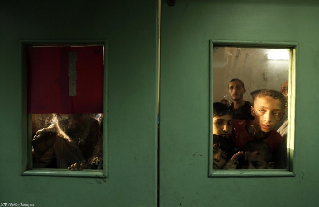 Palestinians look through the doors at Kamal Adwan hospital, where victims were brought following an Israeli strike on a UN school in Jabalia refugee camp 