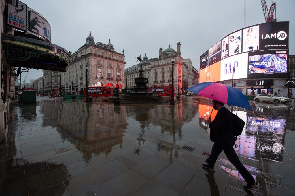 A man with an umbrella walks through a near empty Piccadilly Circus in London, during England