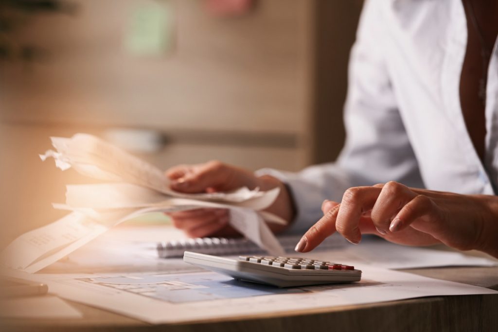 Close up of businesswoman using calculator while going through financial bills.